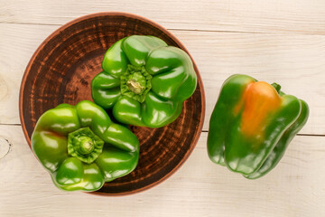 Three sweet green peppers with ceramic plate on wooden table, macro, top view.