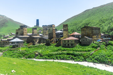 Sticker - Ushguli village in a gorge between mountains. Green fields with yellow flowers, a flowing river. Medieval stone towers and residential houses