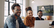 © btiger - Diverse business team laughing and collaborating in modern office with laptop and natural light