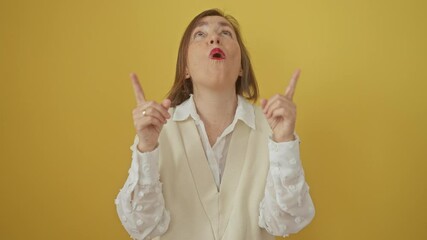 Wall Mural - Amazed middle age hispanic woman, standing and pointing up in surprise, looking with finger on isolated yellow background