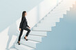 © Who is Danny - Attractive young businesswoman climbing white stairs and concrete wall. Success, worker, career growth and up concept.