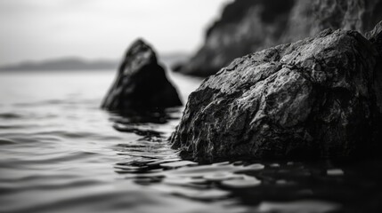  A monochrome image of a rock submerged in water, with a prominent larger one emerging from the surface