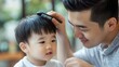 © uros - An Asian young father is combing his little son's hair at home. Toddler boy hairstyle grooming, barber for children. Hairdresser, scissors cutting, face beauty. Parenthood, childhood.Fashion for kids