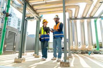 Wall Mural - Professional Asian man and woman teamwork engineer in safety uniform working at outdoor construction site rooftop. Industrial technician worker maintenance checking building exterior plumbing systems.