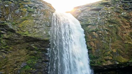 Wall Mural - water is falling down a rocky cliff covered with moss, creating a powerful waterfall on a sunny day.