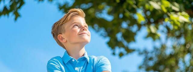 Wall Mural -  A young boy stands before a tree, gazing upward at the sky He folds his hands in front of him