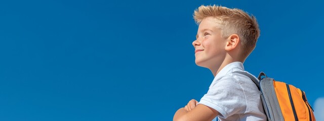 Wall Mural -  A young boy, blond haired, clad in a white shirt, carries a yellow backpack against a backdrop of a clear blue sky