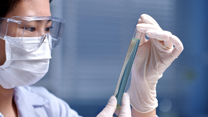 Experiment theme advertising photo was taken from frontal shot on laboratory , female scientist wearing white medical gloves and protective glass, holding a light blue essence test tube for analyzing