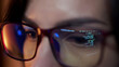 © wedmoments.stock - Close-up of a developer wearing glasses, coding on a computer. Code and analytics reflections in the glasses emphasize focus on cybersecurity and software development.