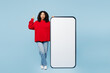 © ViDi Studio - Full body smart little kid teen girl wear red sweatshirt big huge blank screen area mobile cell phone smartphone point index finger up isolated on plain blue background. Childhood lifestyle concept.