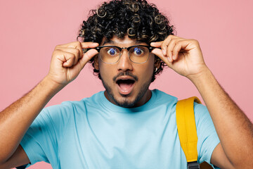 Wall Mural - Young smart shocked surprised Indian boy student wear blue t-shirt casual clothes backpack bag hold touch glasses look camera isolated on plain pink background. High school university college concept.