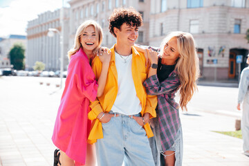 Wall Mural - Group of young three stylish friends posing in the street. Fashion man and two cute female dressed in casual summer clothes. Smiling models having fun. Cheerful women and guy outdoors