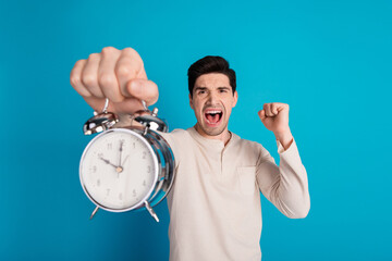 Poster - Photo of nice young man hold alarm raise fist wear pajama isolated on blue color background