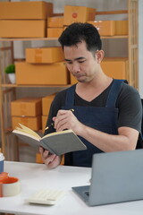 Young Asian man packs parcels for customers Electronic commerce, online shopping, SME business concept. A man holds a package box preparing to send it to a customer.