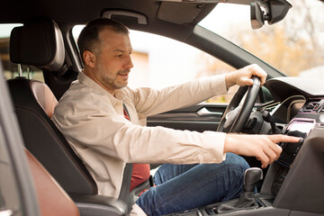 Side view of European man pressing buttons or scrolling on touch screen monitor in his luxury car