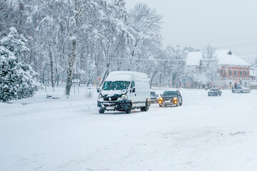 Cars driving on a slippery snowy road on a city street during a heavy snowfall in the evening in winter. Traffic disruption due to blizzards and blizzards. Weather forecast