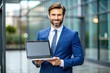 © Four888 - Professional man in a blue suit holds a laptop with a blank screen, ideal for illustrating digital products, software, and websites in a business setting.