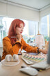 © wattana - Young stylish woman, graphic designer with red hair examining a color swatch in a creative office.