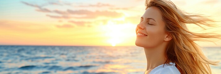 Woman enjoying the refreshing sea breeze at sunset, facing the ocean with closed eyes and a serene smile on the beach.