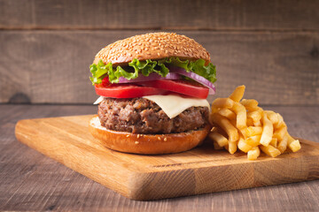 Homemade delicious hamburger with beef, onion, tomato, lettuce and cheese. Fresh burger close up on wooden rustic table with potato fries. Cheeseburger. Burger.