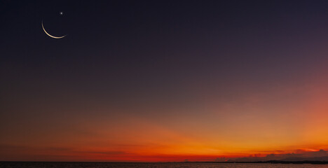 Wall Mural - dusk sky over sea in the evening with orange sunlight after sun down twilight and crescent moon symb