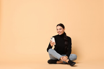 Canvas Print - Smiling woman with smartphone on beige background. Space for text