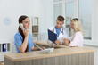 © New Africa - Professional receptionist and doctor working with patient at wooden desk in hospital