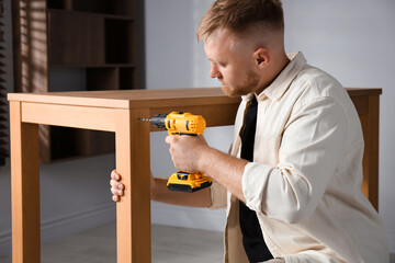 Poster - Man with electric screwdriver assembling table indoors