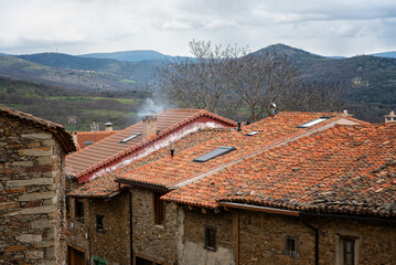 Wall Mural - A row of stone houses with red roofs and mountains in the background. The houses are old and the roofs are made of clay tiles, La Hiruela, Madrid, Spain.