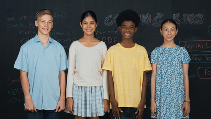 Wall Mural - Group of smart multicultural teenager looking at camera at blackboard. Happy diverse children standing in STEM technology class with engineering code, prompt or planning program idea. Edification.