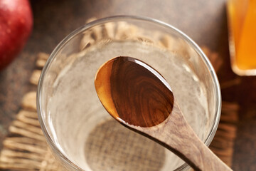 Wall Mural - Apple cider vinegar on a wooden spoon with a glass of water