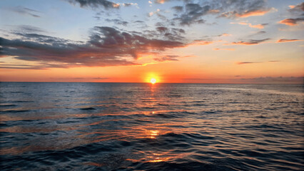 Wall Mural - A beautiful sunset over a calm ocean with the sun dipping below the Horizon