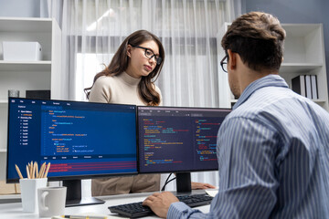 Wall Mural - Woman colleague standing opposite to man programmer working on desk to discuss coding website software system project on two pc screen, comparing with typing full stack data prompt design. Postulate.