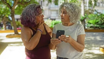 Poster - Elderly women with gray curly hair looking at smartphone in an outdoor park setting during daytime, green trees in the background