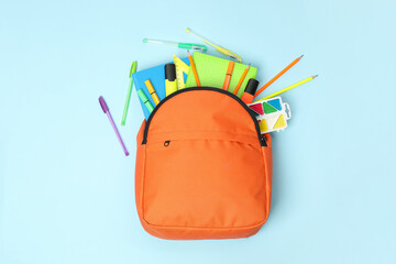 Canvas Print - Orange backpack and different school supplies on light blue background, flat lay