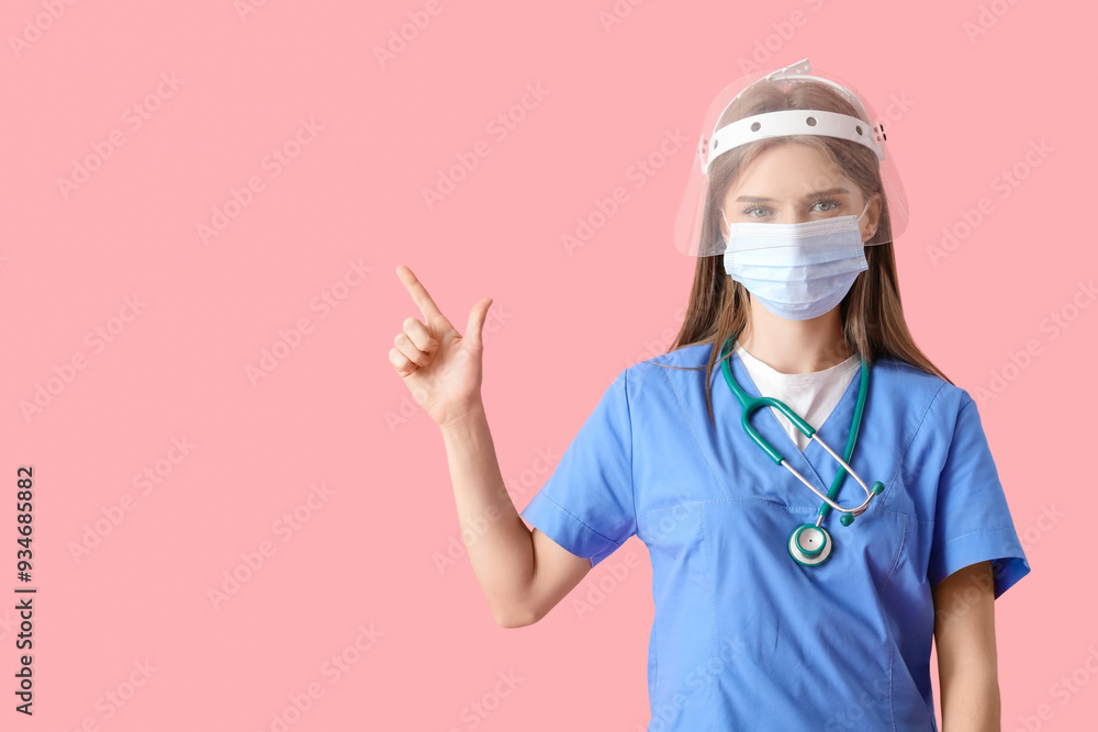 Female doctor in protective masks pointing at something on pink background