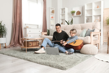 Canvas Print - Private music teacher giving guitar lessons to little boy with online tutorial on laptop at home