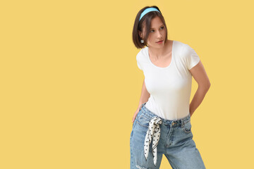 Wall Mural - Beautiful young woman in stylish jeans on yellow background