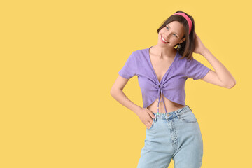 Wall Mural - Beautiful young happy woman in stylish jeans on yellow background