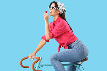 Poster - Beautiful young woman with fresh strawberry and bicycle on blue background