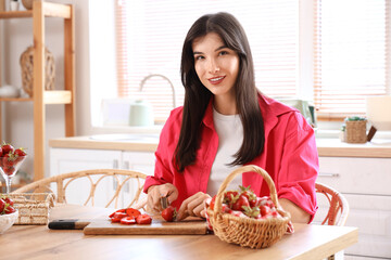 Wall Mural - Beautiful young woman cutting fresh strawberries on table at home