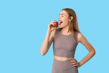 Poster - Sporty young woman eating apple on blue background. Diet concept