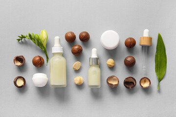 Wall Mural - Macadamia nuts, green leaves, jar and bottles of cosmetic product on grey background