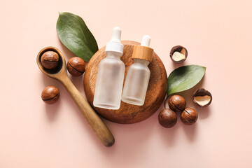 Wall Mural - Macadamia nuts, spoon, wooden stand and bottles of cosmetic product on pink background