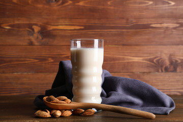 Wall Mural - Glass of fresh almond milk and spoon with nuts on wooden background