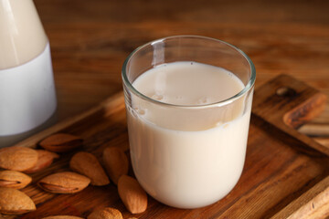 Wall Mural - Glass of fresh almond milk and board with nuts on wooden background