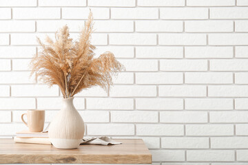 Poster - Vase with dry reeds, books and cup on wooden table against light brick wall