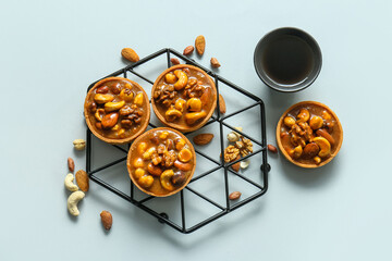 Wall Mural - Tasty tarts with nuts and caramel sauce on stand against grey background