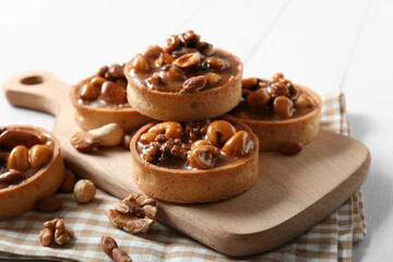 Sticker - Tasty tarts with different nuts and caramel on board against white wooden background