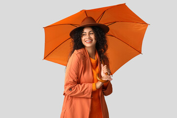 Beautiful young happy African-American woman in autumn outfit with umbrella on grey background